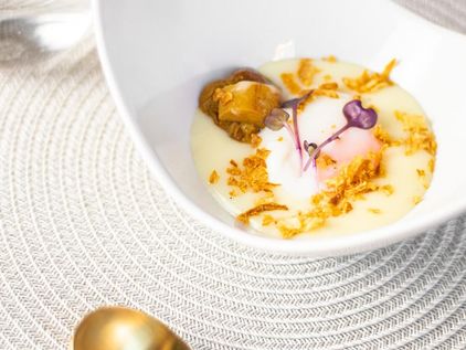 Crema clara con huevo, setas, crujiente dorado y brotes morados, en un cuenco blanco