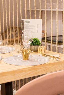 Mesa de madera con un bajoplato blanco y un portavelas dorado, junto a un biombo de cuerdas