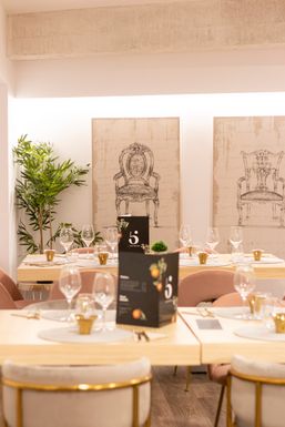 Comedor con las mesas puestas y dos cuadros de sillones al fondo