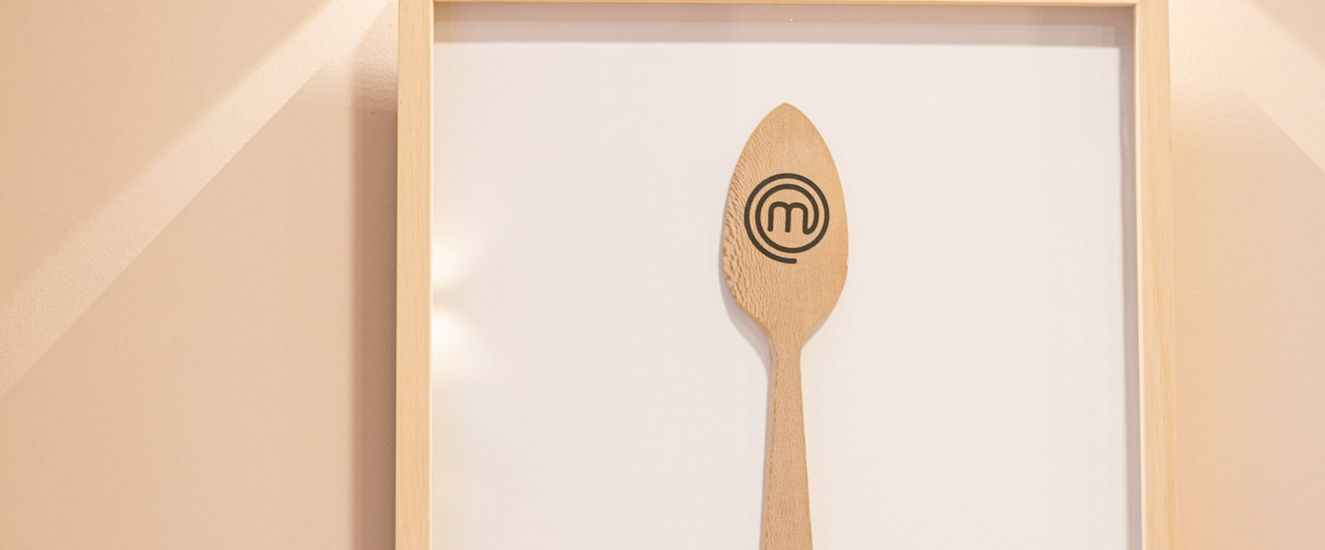 Cuchara de madera con el logo de Masterchef, enmarcada en la pared del restaurante