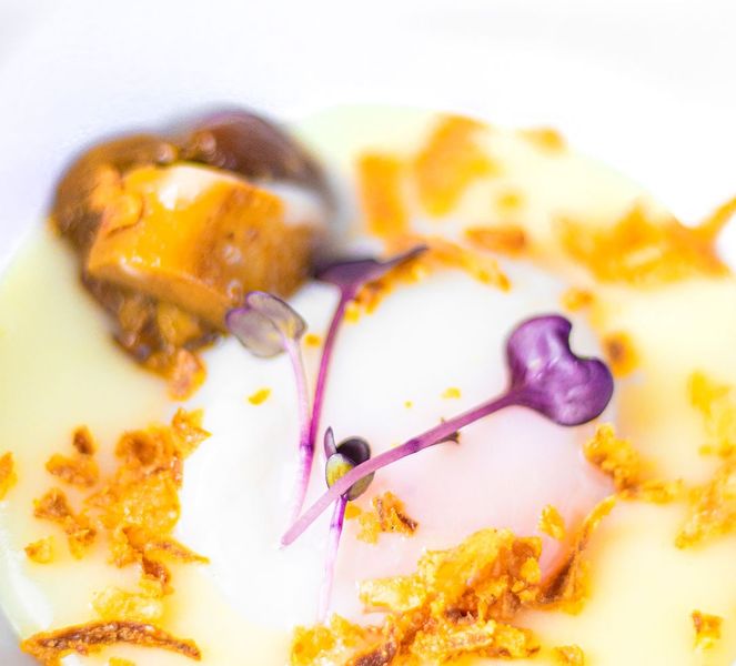 Huevo sobre una crema clara con setas, crujiente dorado y brotes morados